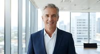 Confident mature Caucasian businessman in navy suit smiling in modern office with city view windows for corporate leadership and professional success concepts.