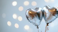 Silver heart-shaped foil balloons against blurred bokeh background with soft glowing lights creating romantic festive atmosphere for celebration events.
