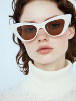 Stylish white cat-eye sunglasses on young woman with natural makeup and curly brown hair wearing cream turtleneck sweater against light background.