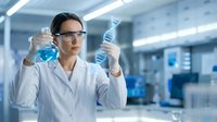 Female scientist in safety glasses examining blue liquid samples in modern laboratory for research and development analysis.