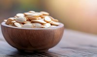 Roasted pumpkin seeds in wooden bowl on rustic table with soft natural lighting and blurred background, healthy snack for nutritious eating.