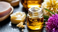 Aromatic essential oil in glass jar with natural ingredients, honey, beeswax and fresh flowers on dark background for spa and wellness treatments.