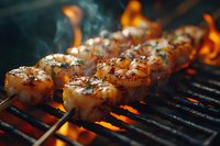 Grilled shrimp skewers with herbs and spices cooking on flaming barbecue grill, close up view with smoke and fire in dark moody atmosphere.