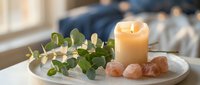 Spa wellness setup with burning candle, eucalyptus branch and pink salt crystals on white plate creating peaceful aromatherapy atmosphere for relaxation and self-care.