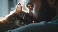 Tender moment between young Caucasian man and sleeping calico cat in soft morning light, showing love and bond between pet owner and feline companion.