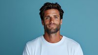 Confident Caucasian man with dark hair and beard wearing white t-shirt smiling against blue background. Professional headshot style portrait showing genuine happiness.