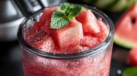 Fresh watermelon smoothie with mint garnish in glass with condensation drops, crushed ice and chia seeds on dark background, refreshing summer drink.
