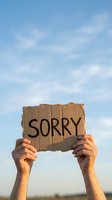 Hands holding cardboard sign with sorry message against blue sky with white clouds for apology and forgiveness concepts.