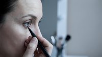 Caucasian middle-aged woman applying black eyeliner pencil close up, beauty makeup routine at home mirror, skincare and cosmetics concept.