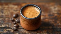 Fresh espresso with creamy crema in traditional clay cup on rustic wooden background with roasted coffee beans, morning coffee concept for cafe menu.