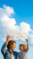 Woman and young child holding YES sign against blue sky with white clouds, representing positive decision, agreement, approval, success, and optimism for advertising and motivational content.