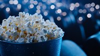 Fresh popcorn in blue metallic bucket against dark background with bokeh lights creating cinematic atmosphere for movie night entertainment.