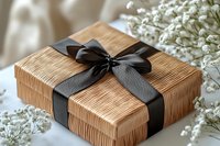Elegant gift box wrapped in textured kraft paper with black satin ribbon bow, decorated with delicate white baby's breath flowers on neutral background.