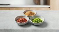 Three ceramic bowls with colorful spices and herbs arranged on modern kitchen counter for culinary cooking and food preparation.