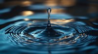 Macro photography of water drop impact creating symmetrical ripples and crown splash formation against dark turquoise background with dramatic lighting effects.