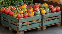 Fresh heirloom tomatoes in varied colors and sizes displayed in rustic turquoise wooden crates, showcasing organic farm produce at local market.