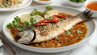 Grilled whole fish with spicy tomato sauce, herbs and vegetables on white plate. Traditional seafood dish for restaurant menu and culinary photography.