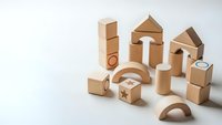 Natural wooden building blocks set with geometric shapes including cylinders, cubes, arches and triangular pieces arranged on white background for educational play.