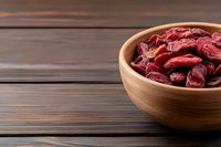 Dried cranberries in wooden bowl on rustic wood table background for healthy snacking and cooking ingredients.