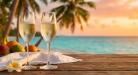 Two champagne glasses on wooden table with tropical beach sunset background and palm trees for romantic vacation celebration.