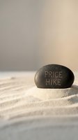 Price hike text engraved on dark stone resting on sand with soft neutral background, symbolizing cost increase and inflation concept for business and economics.