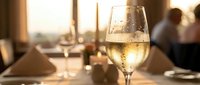 Glass of white wine on elegant restaurant table during golden hour sunset creating warm atmospheric dining ambiance for romantic evening celebration.