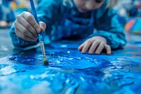 Young child painting with blue watercolors on paper, close-up view of hands holding brush. Creative arts education and early childhood development concept.