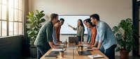 Diverse business team collaborating around conference table in modern office with natural light and plants for corporate meetings and teamwork presentations.