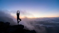 Woman practicing yoga tree pose on mountain cliff at sunrise with misty valley below. Meditation and wellness lifestyle concept for mindfulness and spiritual balance.