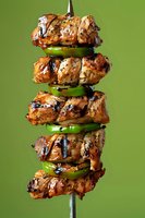 Grilled chicken kebab skewer with green bell peppers, marinated in herbs and spices, showing char marks and caramelization against green background.