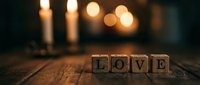Wooden letter cubes spelling LOVE on a rustic table with glowing candles and warm bokeh lights in the background.