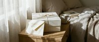 Elegant gift box with twine bow and thank you card on wooden nightstand in cozy sunlit bedroom interior styling.