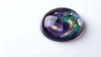 Galaxy swirl resin art pendant with cosmic colors purple green gold isolated on white background for jewelry making crafts and accessories design.