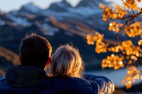 Romantic couple watching sunset in mountains, backlit by golden autumn leaves. Intimate moment with warm evening light creating magical atmosphere.