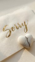 Gold calligraphy sorry card with marble heart stone on cream paper, soft sunlight, apology and forgiveness concept for greeting design.