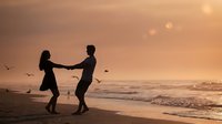 Romantic couple silhouettes holding hands dancing on beach at golden sunset with ocean waves and seagulls flying in warm evening light for love concepts.