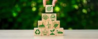 Hand arranging wooden blocks with green environmental icons including recycling, renewable energy, and sustainability symbols on natural background.