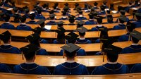 Graduation ceremony with rows of students in blue caps and gowns sitting in wooden auditorium seats, academic achievement and education milestone.