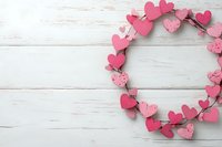 Pink and coral heart shapes arranged in circular wreath pattern on white rustic wooden background with copy space. Romantic holiday layout for Valentine's Day designs.