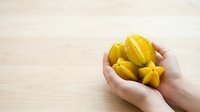 Fresh yellow star fruit held in hands on wooden surface, tropical fruit for healthy eating and nutrition content.