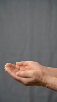 Elderly hands cupped together in receiving gesture against blurred gray background showing age, wisdom, care and support concepts for healthcare design.