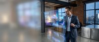 Middle-aged Caucasian male businessman in formal attire analyzing digital financial data displayed on transparent screen in modern office setting with city skyline view.