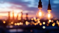 Glowing vintage light bulbs hanging against blurred city sunset skyline with warm bokeh lights creating atmospheric urban evening ambiance.