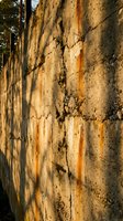 Weathered concrete wall with rust stains and cracks in warm sunlight creating textured urban decay background for industrial design projects.