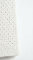 White embossed dot pattern on soft tissue paper roll with textured surface and shadow detail against neutral background.