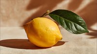 Fresh yellow lemon with green leaf on beige fabric background, casting soft shadow. Natural citrus fruit for cooking, beverages, and healthy lifestyle concepts.