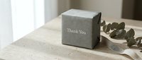 Gray textured gift box with Thank You text on wooden surface, eucalyptus leaves and ribbon, elegant minimal packaging for gratitude and appreciation.