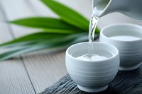Pouring fresh water into ceramic bowl on wooden surface with green bamboo leaves creating peaceful spa atmosphere for wellness and relaxation rituals.