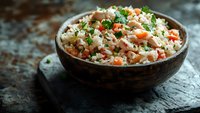 Homemade rice pilaf with diced vegetables and fresh herbs served in rustic wooden bowl on dark textured background, close up view with selective focus.