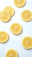Fresh lemon slices scattered on a white wet surface with water drops, bright yellow citrus fruit flat lay for food and drink design.